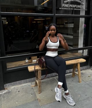 Coco is wearing a white sports bra, black leggings, gray New Balance sneakers, and a burgundy Saint Laurent bag.