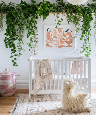 A unisex nursery painted pale gray, with white furniture, hanging plants and a toy alpaca.