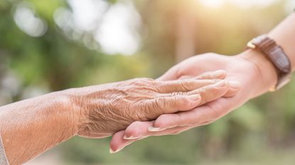 An older adult rests their hand in the hand of a younger person in a caring gesture.