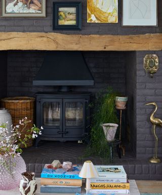 large open fireplace with a log burner surrounded by antique and vintage art and a coffee table with books and decor