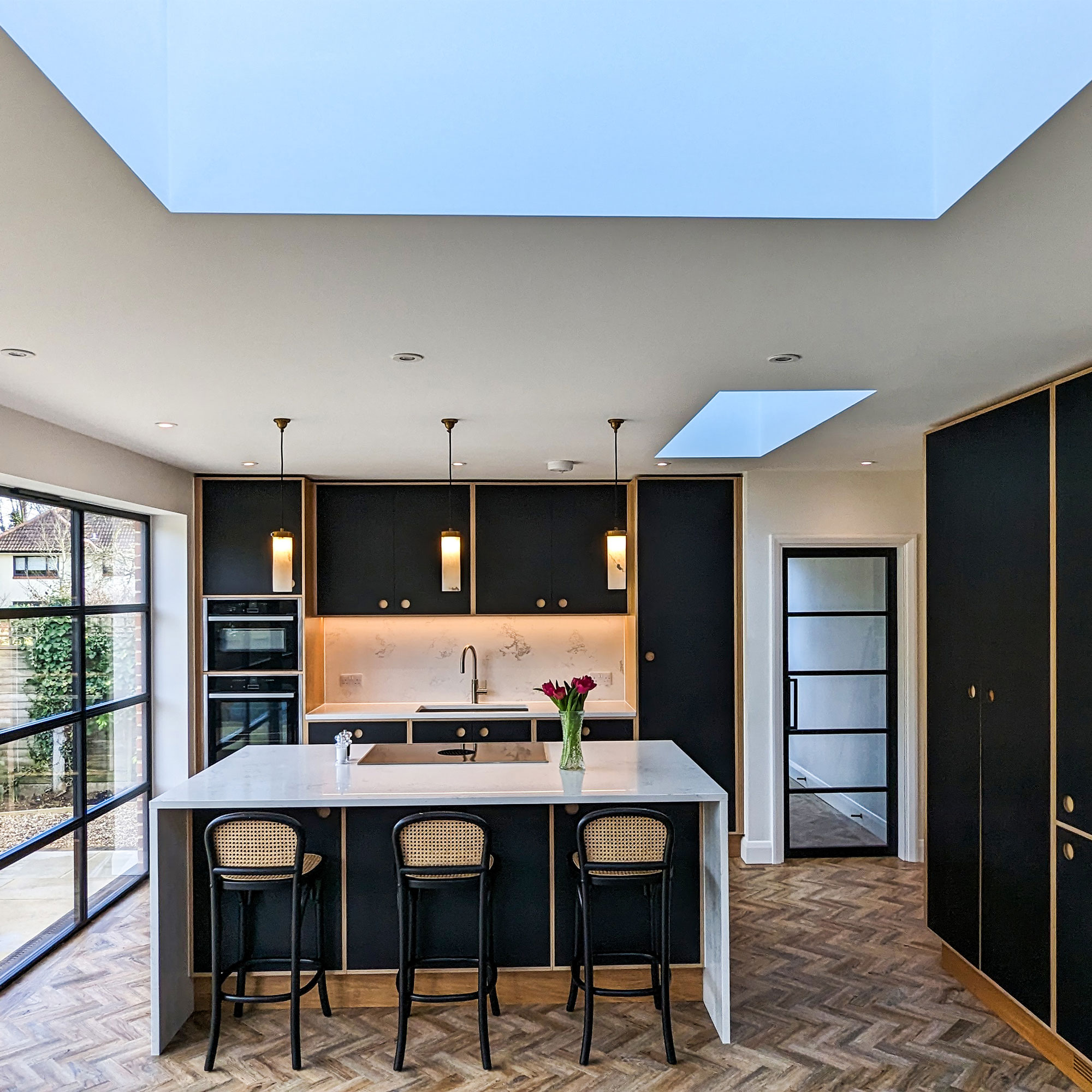 modern black kitchen in extension with roof lantern and herringbone wooden flooring