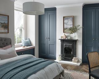A blue bedroom with fitted wardrobes, double bed and window seat