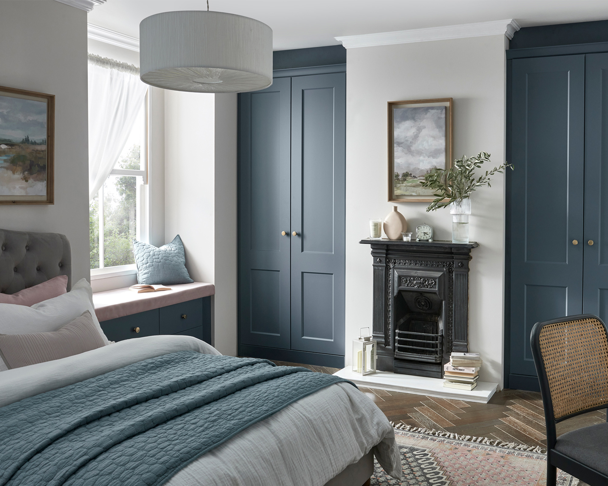 A blue bedroom with fitted wardrobes, double bed and window seat