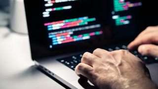 A man on a laptop, close on the hands hovering over the keys
