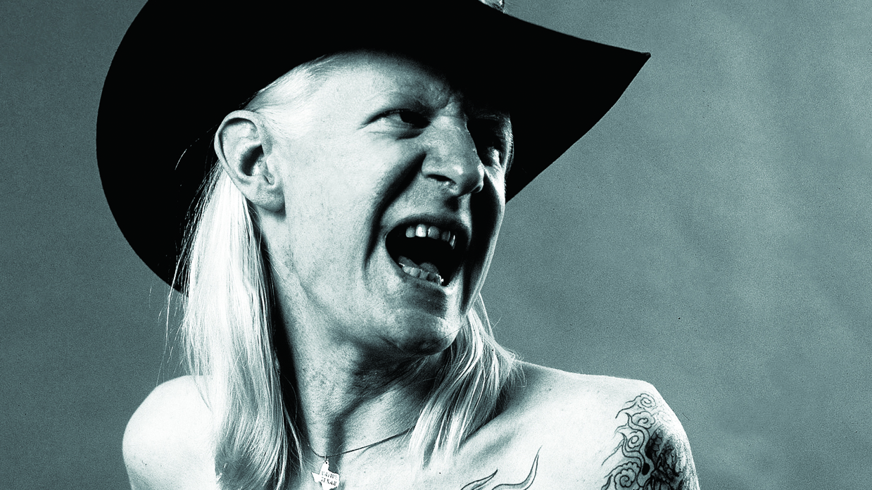 Johnny Winter, yelling, topless, wearing a cowboy hat.