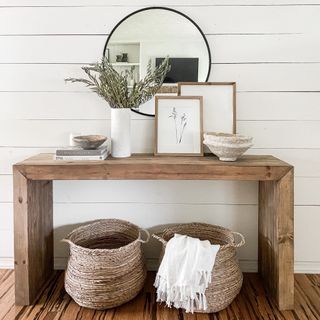 Wooden entryway console table topped with frames and baskets placed underneath