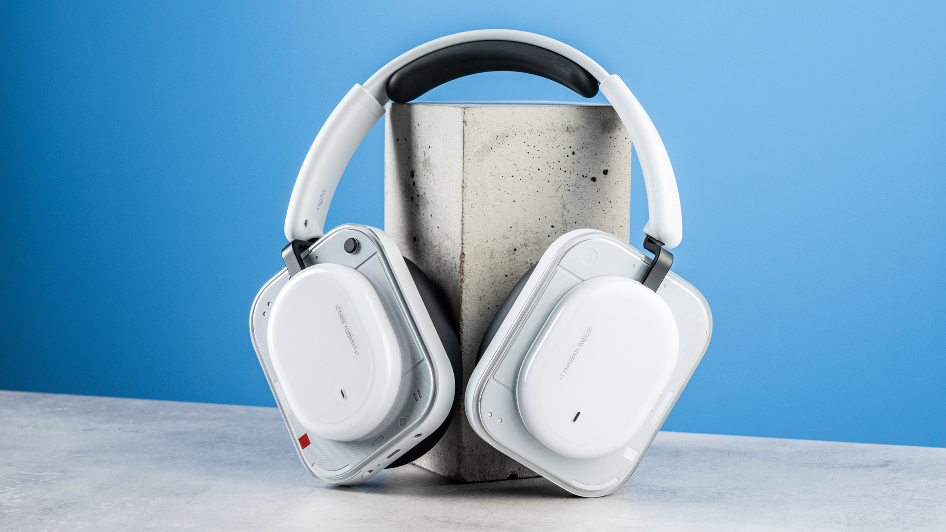 the nothing headphone (a) photographed against the blue tom's guide background, showing the transparent and white ear cups with red accents, the padded headband, and the accessories including 3.5mm jack