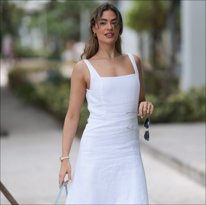 Jessica De Oliveira seen wearing gold earrings, Riani white strappy long dress, Jacquemus light blue suede leather Bambino Long bag, Dior gold cat-eye sunglasses, on December 09, 2023 in Miami, Florida. 