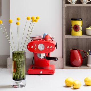 Red espresso machine on a white worktop in a white kitchen with yellow accents