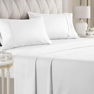 CGK Unlimited Store Queen Size 4 Piece Sheet Set on bed with shams, quilted headboard and white nightshade lamp light fixture in background