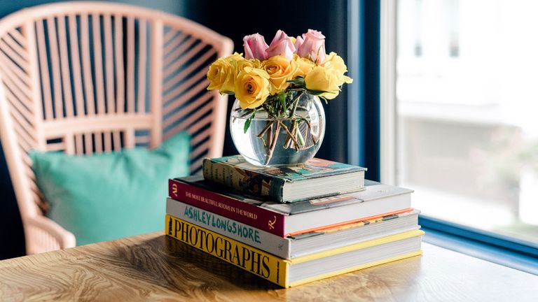 Colorful roses arrangement in round glass vase, on stack of books on coffee table