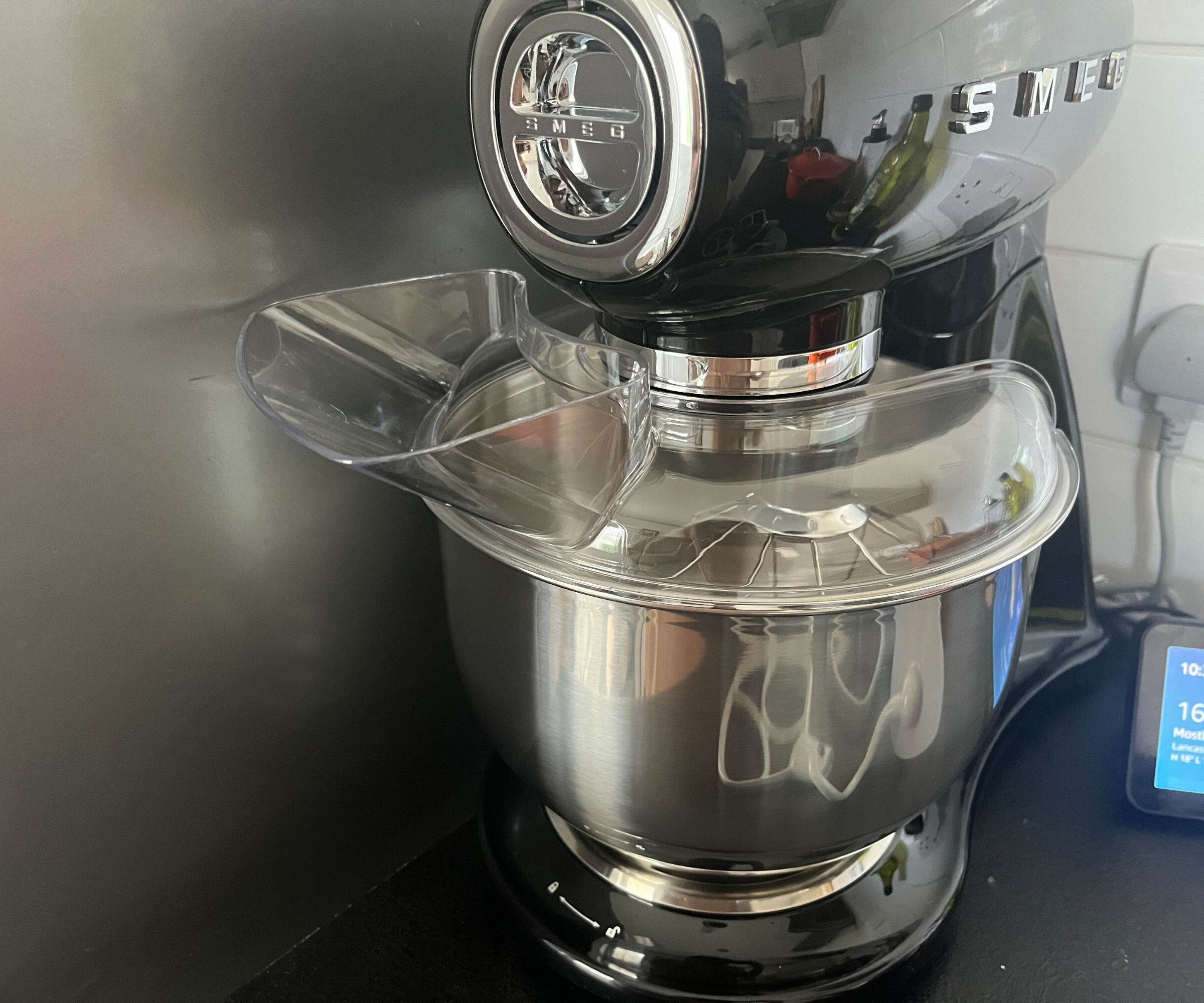 The plastic pouring spout on the stainless steel mixing bowl of a black SMEG stand mixer. 
