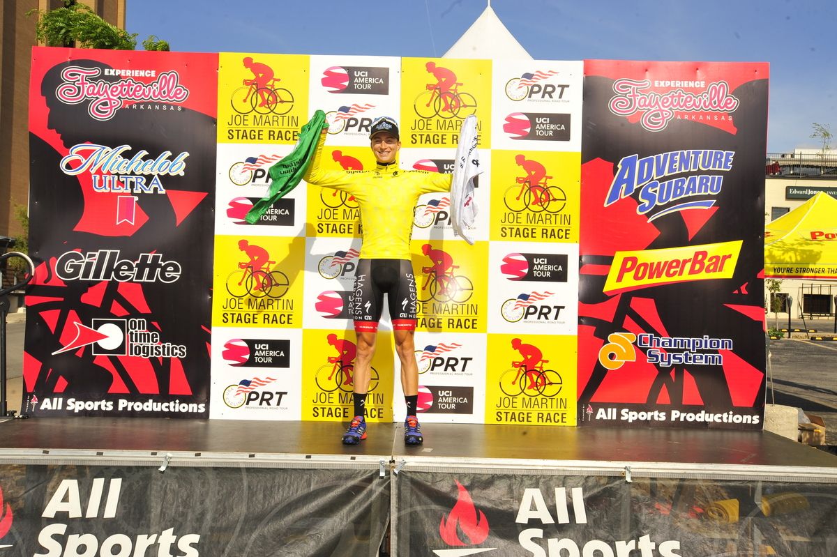 Neilson Powless (Axeon Hagens Berman) holds aloft his young rider and points jerseys while wearing the leader's yellow jersey