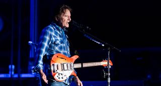 John Fogerty wears a blue plaid shirt and plays his Fireglo 'Acme' Rickenbacker live onstage in 2022