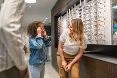 child trying on glasses while adult woman assists at an opticians