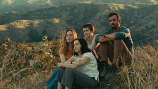 The Mosquito Coast cast sit on the ground in front of a mountain backdrop