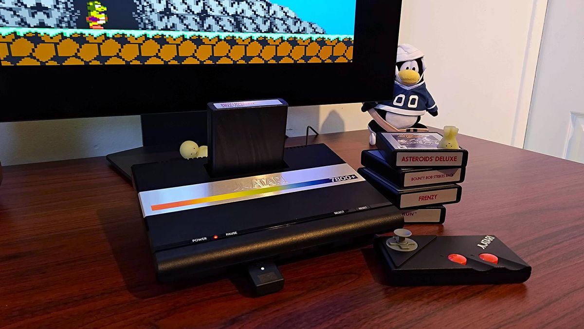 Atari 7800+ sitting on desk connected to monitor next to cartridges and controller with Bentley Bear&#039;s Crystal Quest on screen