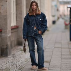 Sophia Geiss is seen wearing various-sized golden hoop earrings, an oversized dark blue denim jacket with a brown faux fur collar from Worst Behavior, matching straight-legged jeans with orange decorative seams also from Worst Behavior, a rectangular brown logo-patterned vintage handbag from Fendi, oval rimless black sunglasses from Vehla Eyewear in her hand, and sand-colored platform shoes from Ugg on September 26, 2024 in Berlin, Germany. (Photo by Jeremy Moeller/Getty Images)