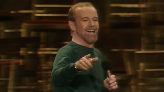 George, dressed in green, smiling on stage, footage from HBO's Doc George Carlin's American Dream.