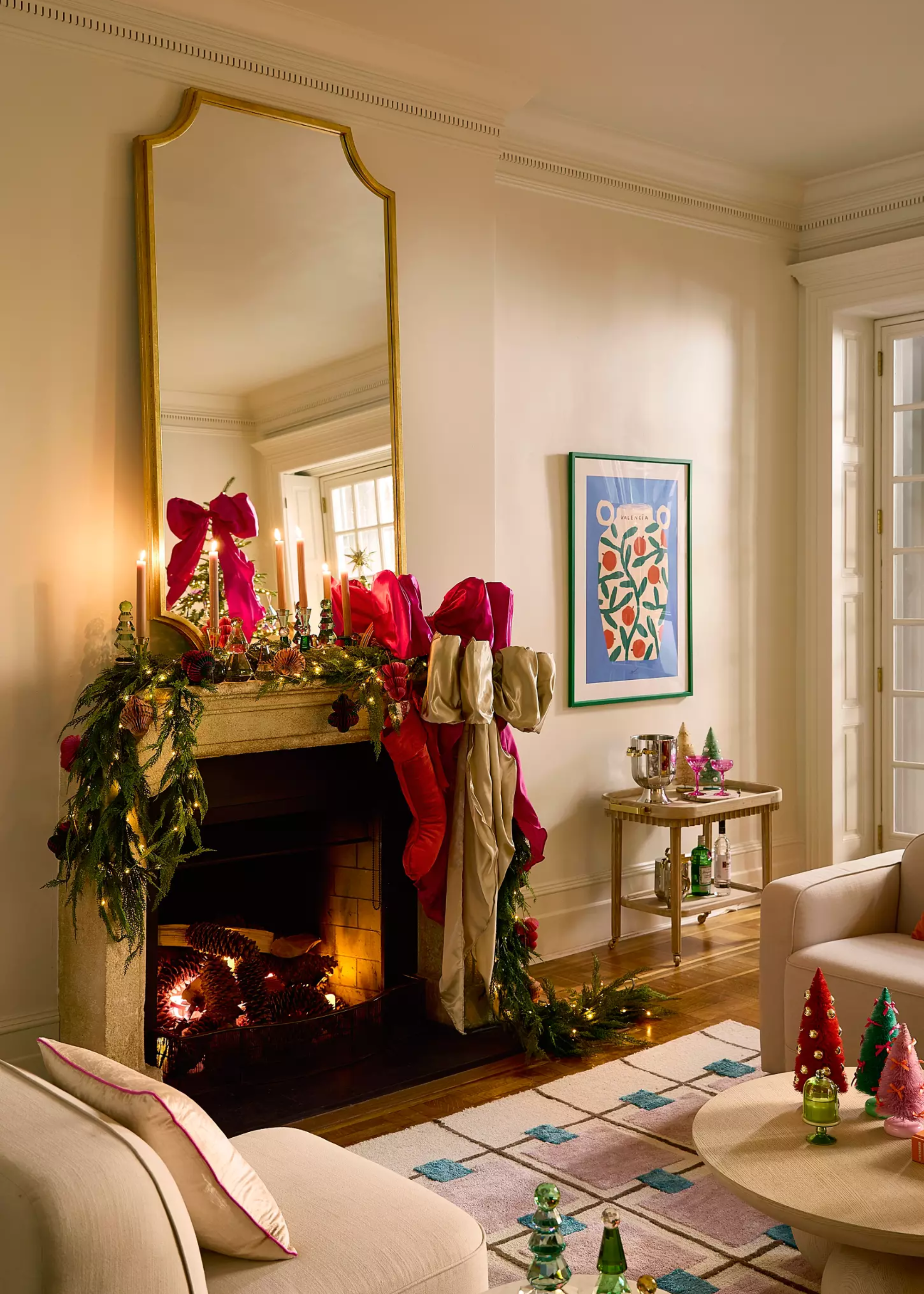 Anthropologie&#039;s giant bows used as Christmas mantel decor among a festive garland in front of a large gold-framed mirror with a lit fire underneath