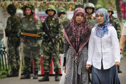 Ethnic Uyghur women pass Chinese military members.