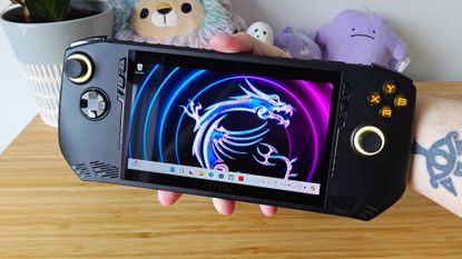 Hand holding MSI Claw AM1 handheld next to woodgrain unit.