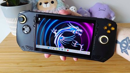 Hand holding MSI Claw AM1 handheld next to woodgrain unit.