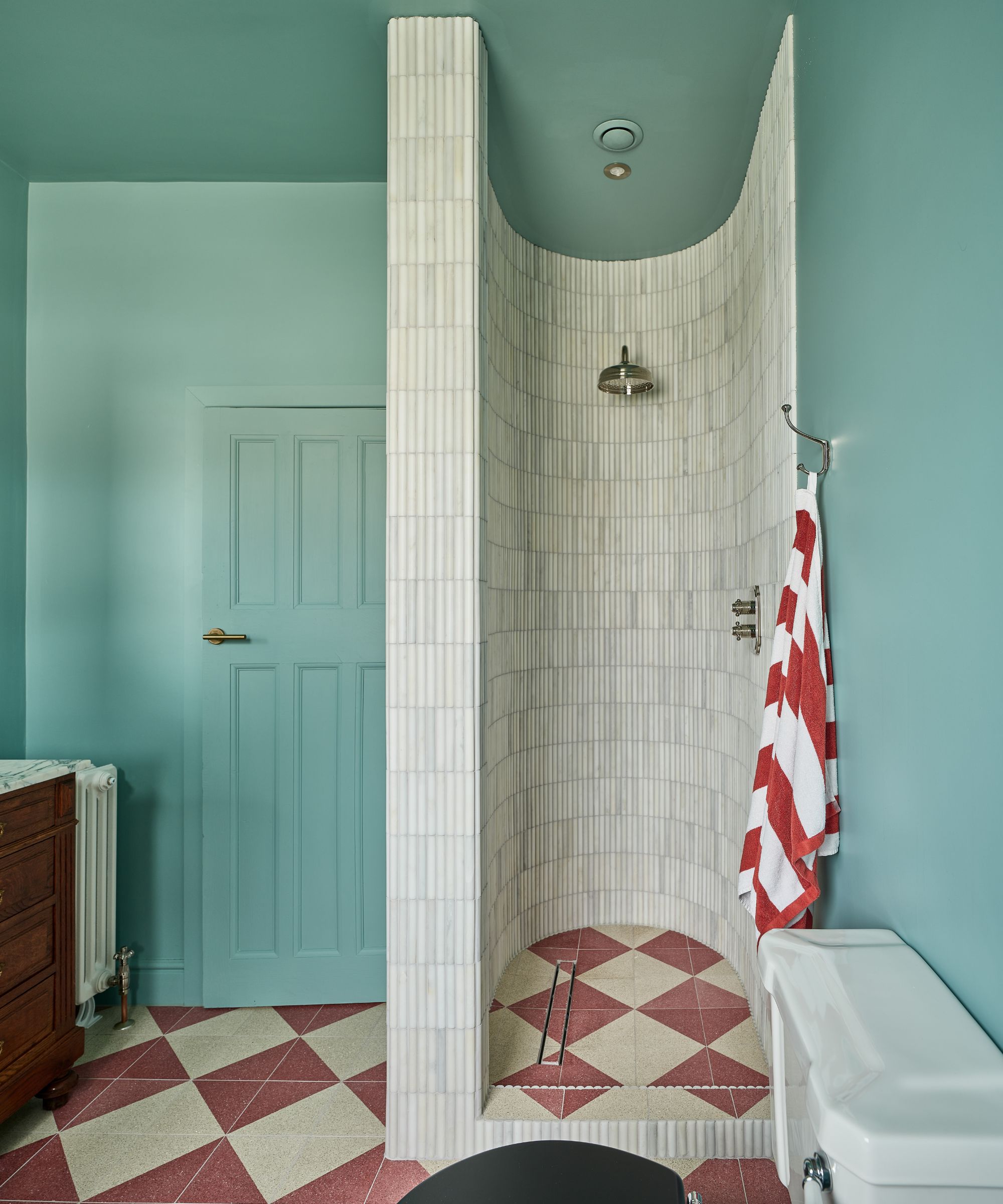 A Bathroom color drenches in light blue with white and red checkerboard floor tiles and a curved shower nook with white tiles