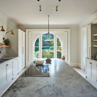Large kitchen in period homes with marble topped island, cream units and arched window