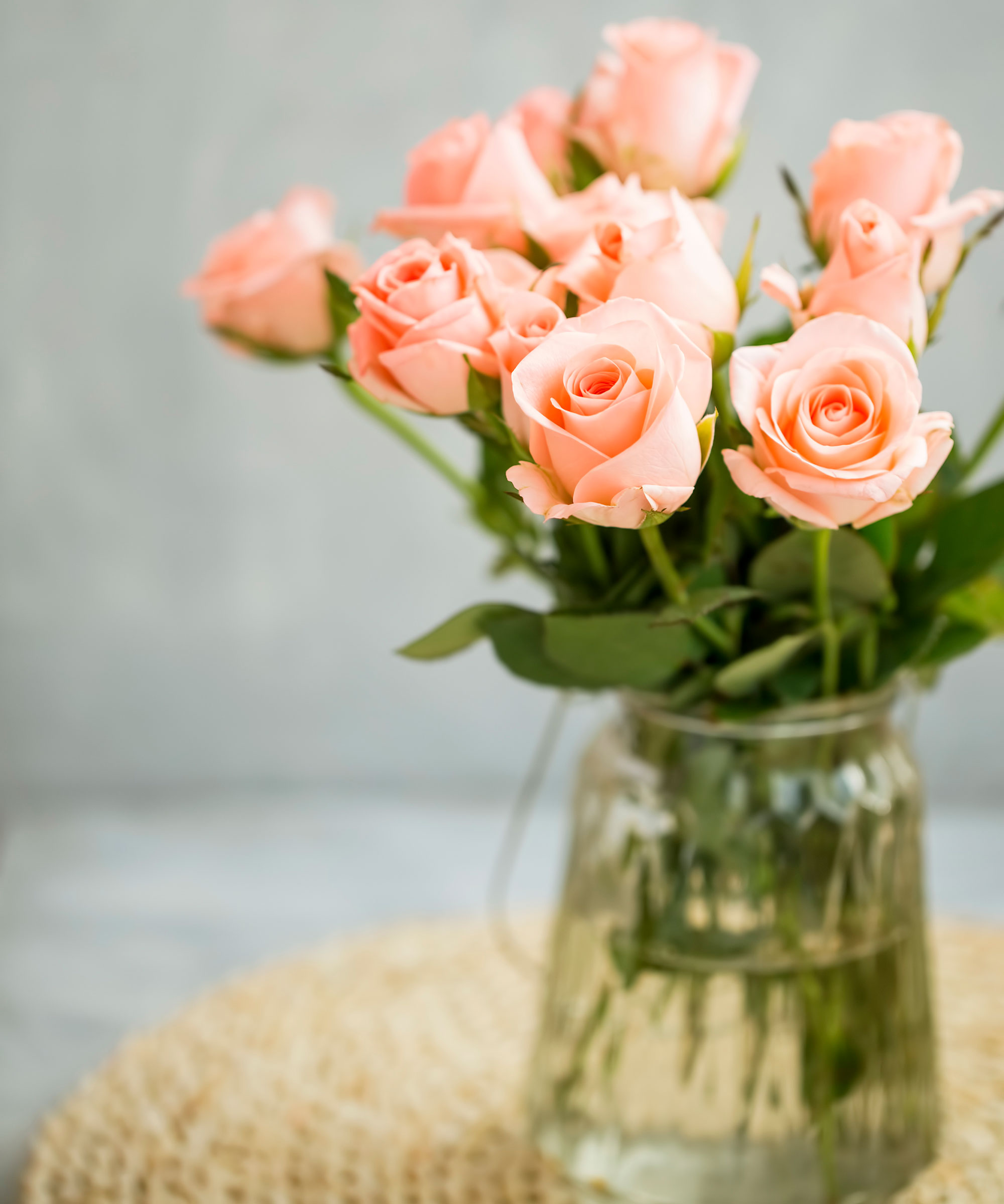 peach roses in glass vase on rattan table mat
