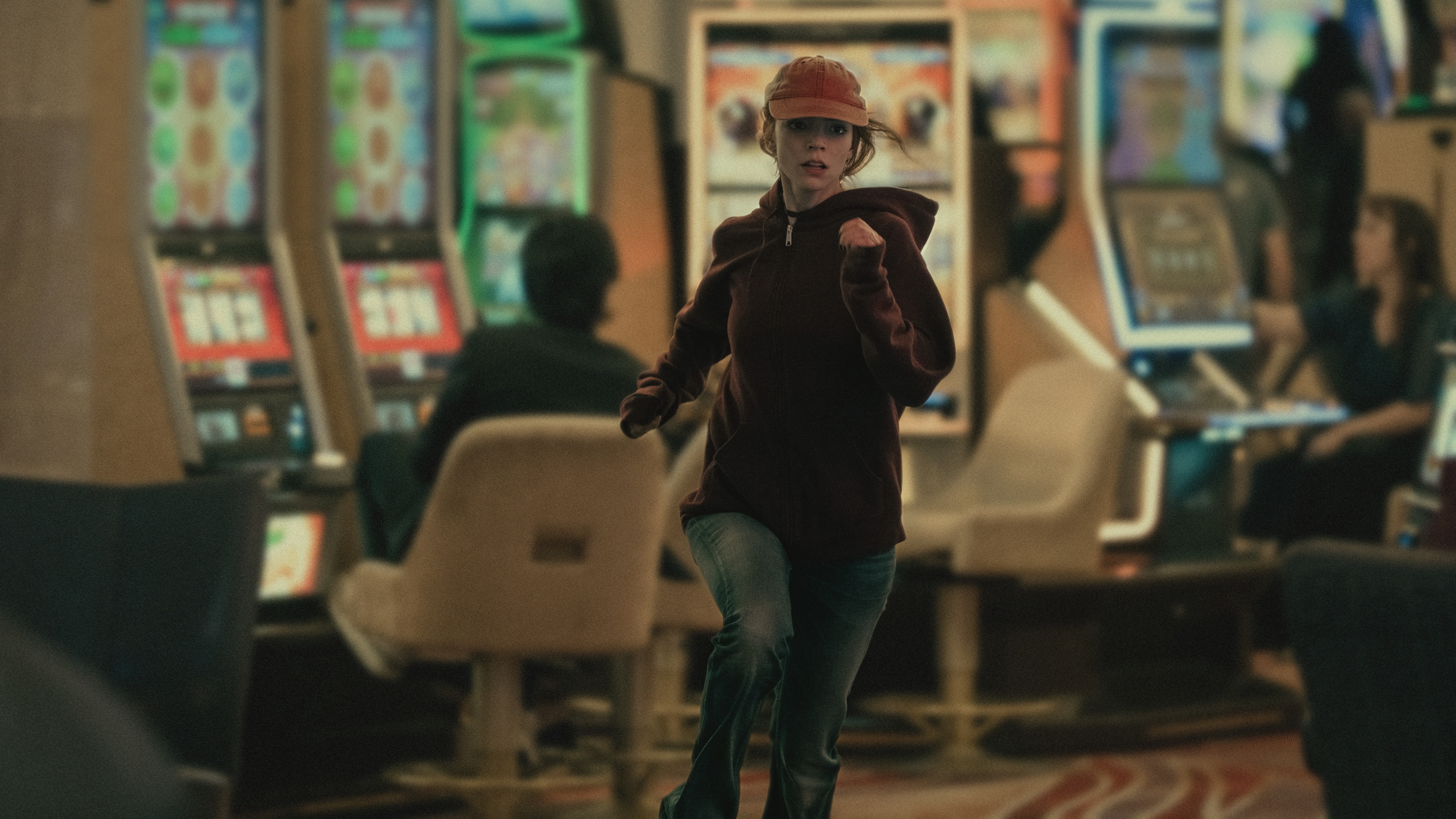 Lucky (Anya Taylor-Joy) running through a casino wearing a baseball cap and burgundy sweatshirt.
