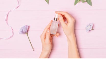 woman holding dropper of serum on pink backdrop with flowers