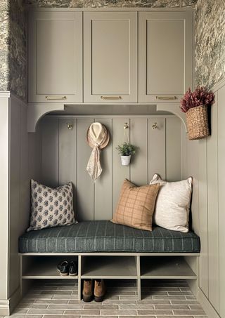 Image of a greenish gray mudroom with a built-in shoe bench, wood paneling, and cabinetry.