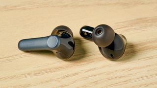 A photo of the EarFun Air Pro 4 earbuds out of their case on a wooden surface