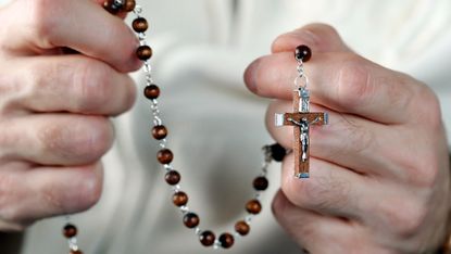Close up of the hands of Catholic man praying with prayer beads