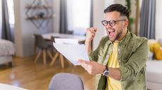 A man celebrates as he looks at paperwork in his home.