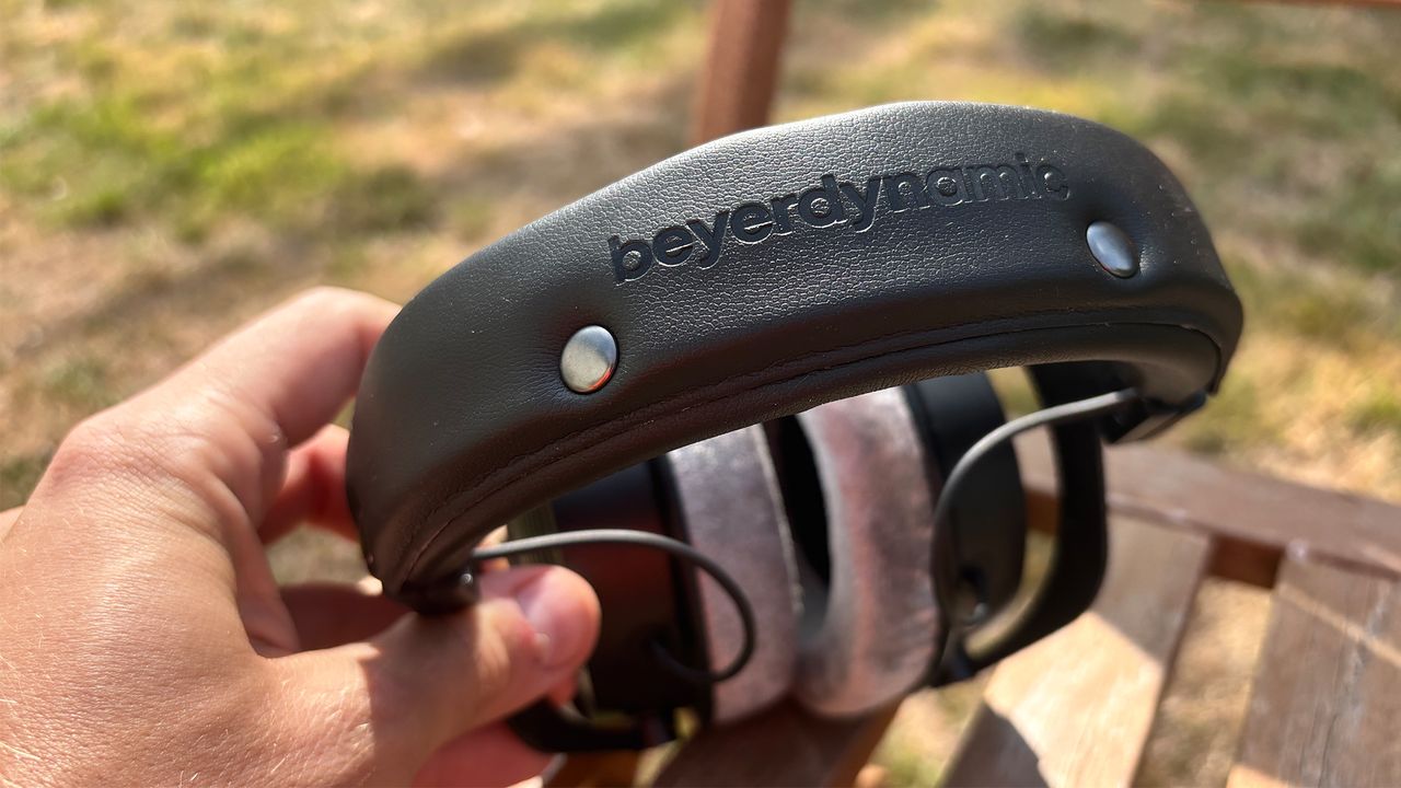 The Beyerdynamic DT 990 Pro X wired headphones shot from above while held in the hand, showing the 'Beyerdynamic' logo on the top of the headband.