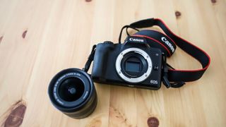 Kameraet Canon EOS M50 Mark II på et tregulv ved siden av et 11-22 mm-objektiv.