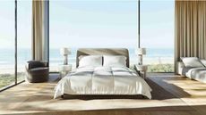 Saatva bedframe in a large bright bedroom with floor-to-ceiling windows with a beach behind. The flooring is light wood, and either side of the bed are two matching white nightstands and lamps.