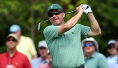 Sir Nick Faldo hits a wedge shot and watches the flight