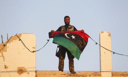 A Libyan rebel holds a Kingdom of Libya flag at Gadhafi's compound in Tripoli