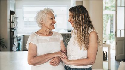 A grandmother and her adult granddaughter stand in a kitchen.