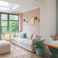 A pastel pink-painted open-plan living room with a cream modular sofa and a rattan chair