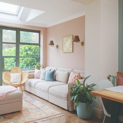 A pastel pink-painted open-plan living room with a cream modular sofa and a rattan chair