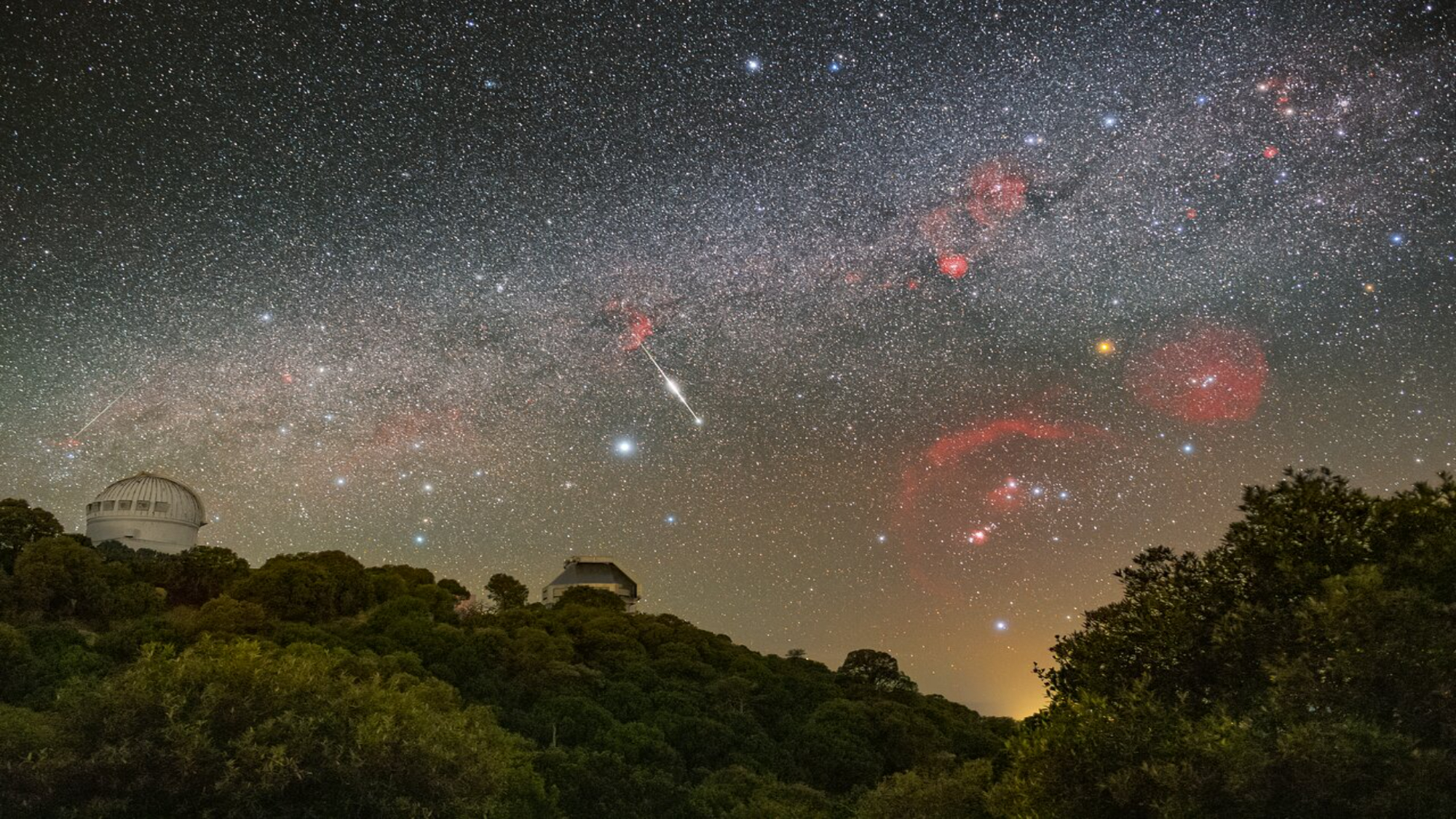 Meteor streaks across the sky above big observatory