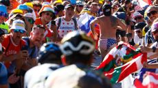 Cycling fan is swimming trunks runs up a climb at the Tour de France flanked by fans