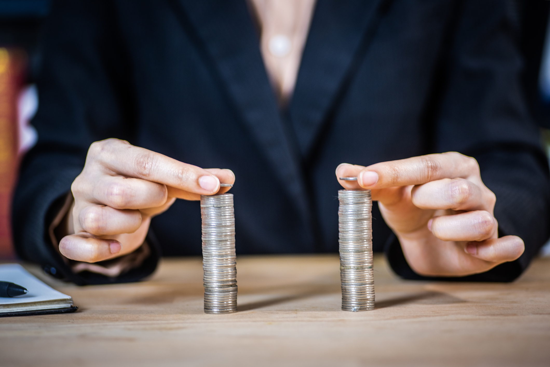 A person in a business suit is placing coins on two equal stacks, representing a 401(k) match.
