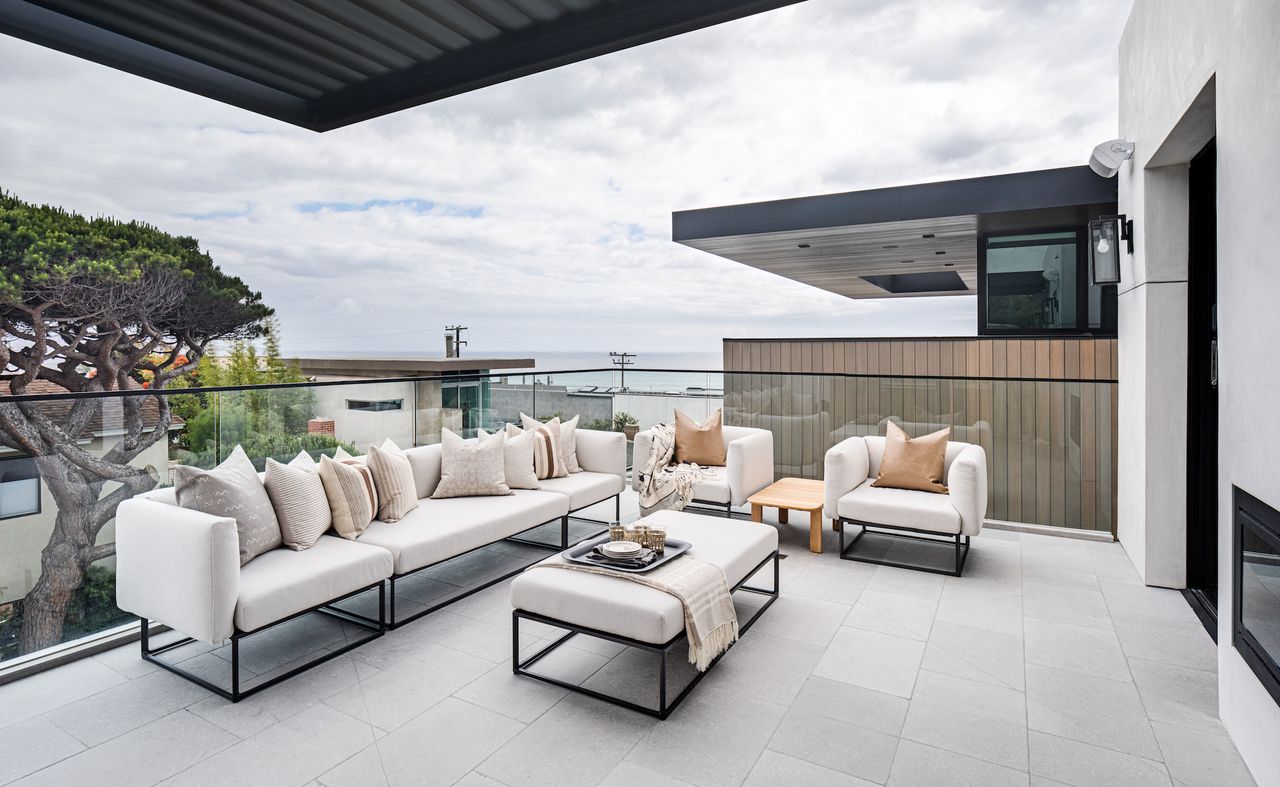 Apartment patio ideas – modern apartment patio with white and metal outdoor sofa and armchairs, view of the sea, pale grey floor tiles, glass panels