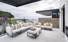 Apartment patio ideas – modern apartment patio with white and metal outdoor sofa and armchairs, view of the sea, pale grey floor tiles, glass panels