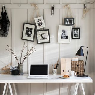 home office with white desk and white wall and picture rail with picture frames and black desk
